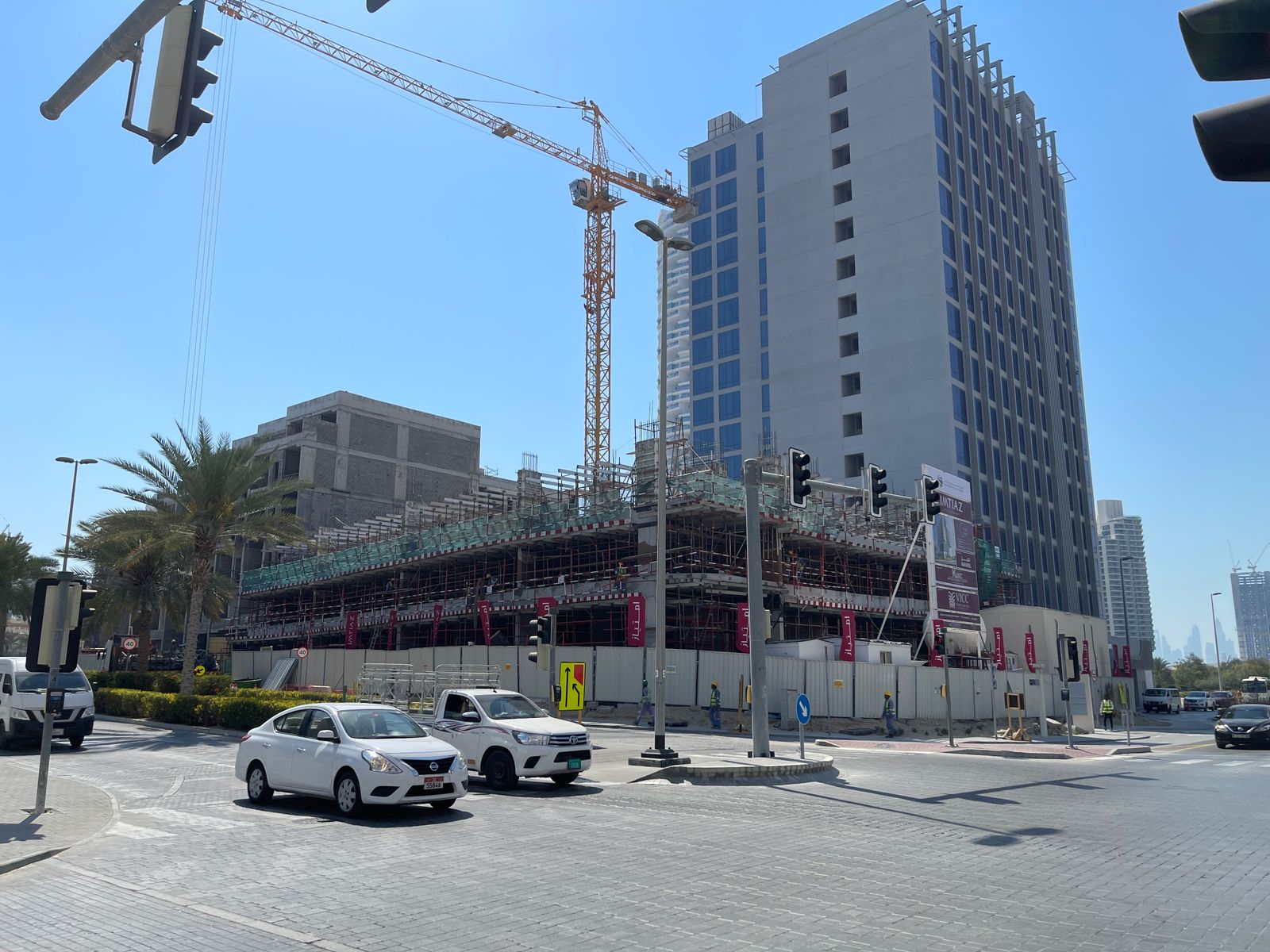 Pearl House By Imtiaz A construction site with a tall building under construction, cranes, traffic lights, and nearby palm trees.